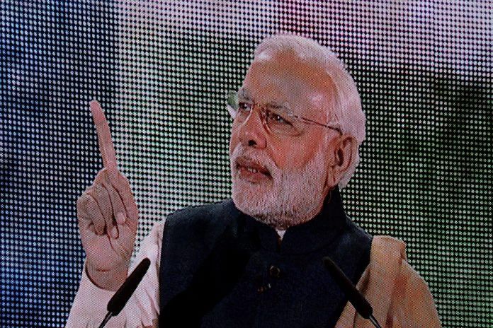 A large screen shows Prime Minister Narendra Modi speaking on stage.
