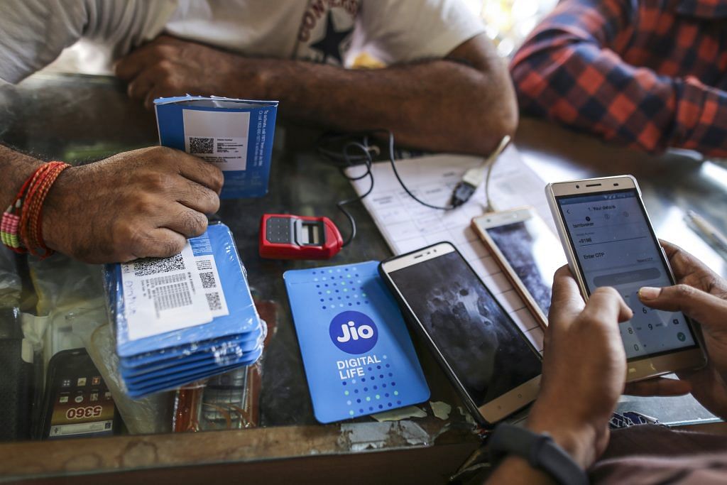 A customer holds a SIM card packet while waiting to connect his mobile phone to the carrier Reliance Jio | Dhiraj Singh/Bloomberg