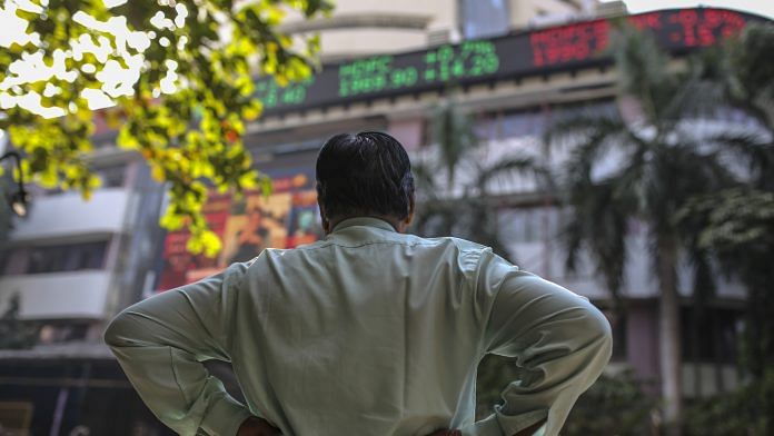 A man stands in front of an electronic ticker board showing stock information figures outside the Bombay Stock Exchange (BSE) in Mumbai | Dhiraj Singh | Bloomberg