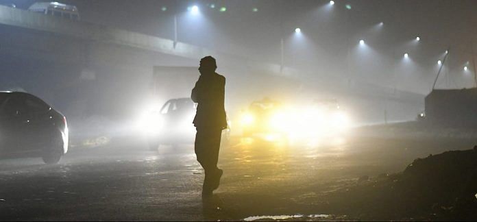 A pedestrian is silhouetted as traffic moves along a road shrouded in smog in New Delhi