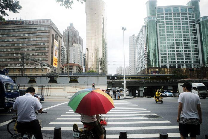 Pedestrians wait to cross a road at a signal light as rain falls in Shenzhen, China