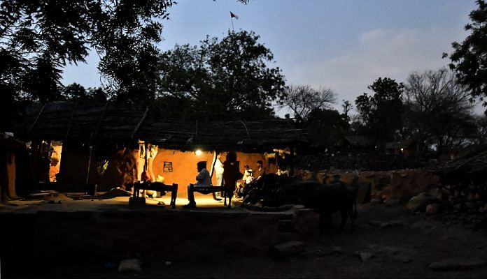 People sit outside a home at dusk in Kraska village, Rajasthan | Anindito Mukherjee/Bloomberg