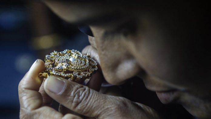 An employee uses a loupe to inspect a diamond studded gold jewelry piece