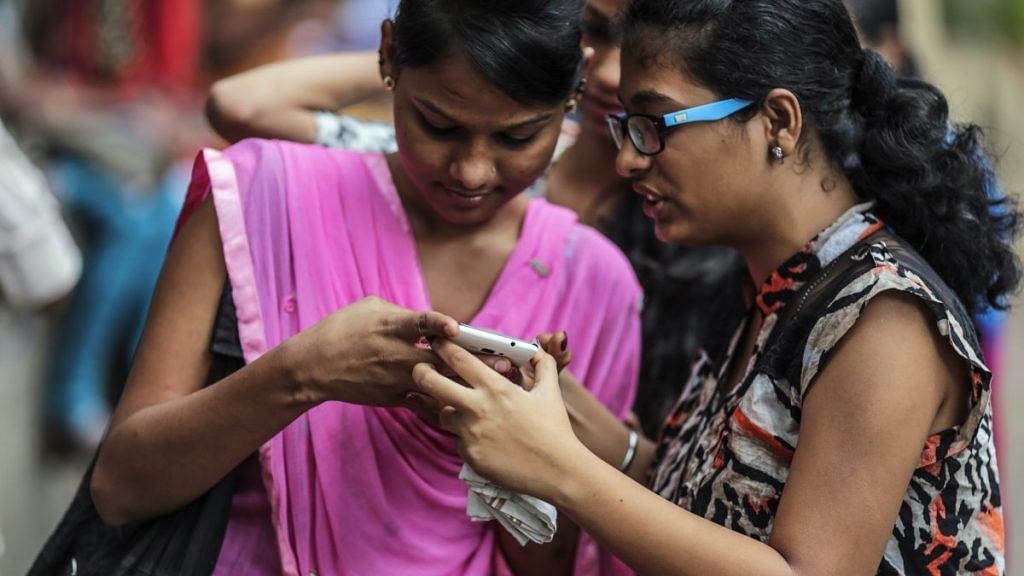 Women in Mumbai look at a phone | Dhiraj Singh/Bloomberg