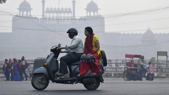 People ride a scooter along a road shrouded in smog in New Delhi