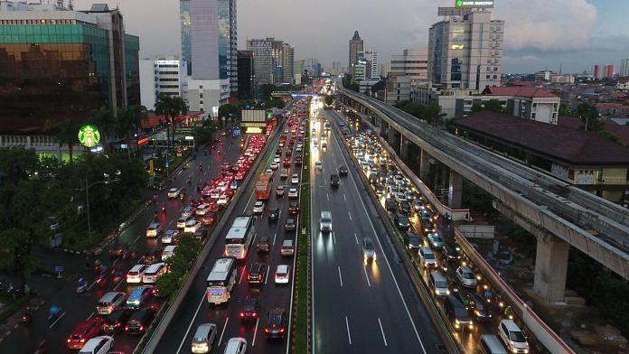 Vehicles travel along a road as an elevated track for the Jakarta Mass Rapid Transit (MRT) rail system, right, stands under construction at dusk in Jakarta, Indonesia