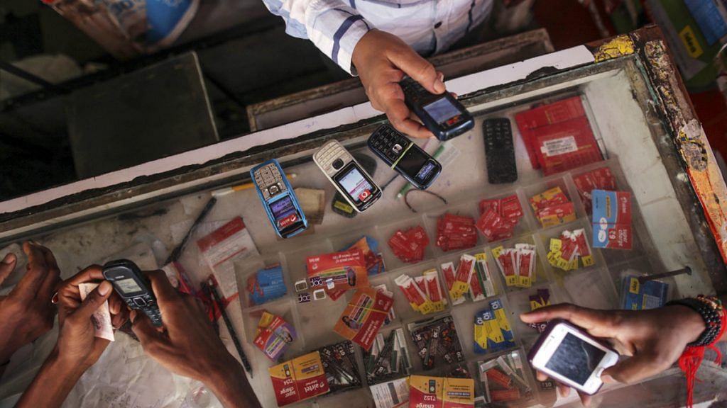 Customers wait to recharge their mobile phones as a vendor checks another device at a mobile phone store in the Dharavi slum area of Mumbai, India, on Tuesday, Aug. 12, 2014