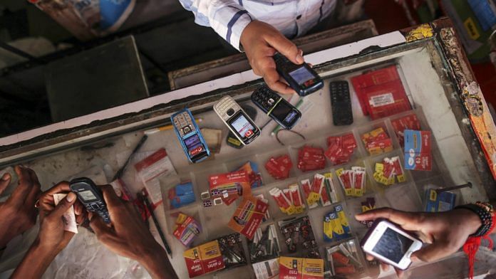 Customers wait to recharge their mobile phones as a vendor checks another device at a mobile phone store in the Dharavi slum area of Mumbai, India, on Tuesday, Aug. 12, 2014