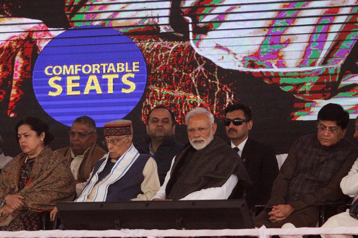 An image of 'comfortable seats' on the express train flashes behind a grim Narendra Modi, who is flanked by senior BJP leader Murli Manohar Joshi (3rd from left) and union minister Piyush Goyal (extreme right)