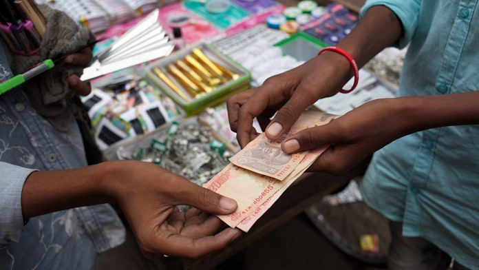 A vendor hands Indian rupee banknotes to a customer at a stall in Chauta Bazaar in Surat, Gujarat