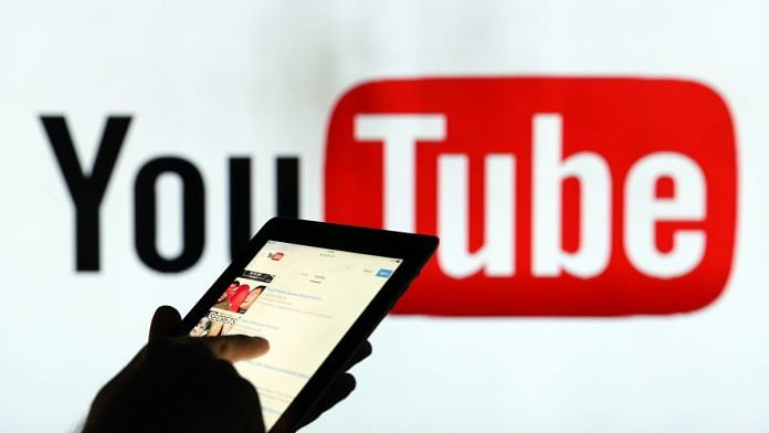 A man is seen as a silhouette as he checks a mobile device whilst standing against an illuminated wall bearing YouTube Inc.s logo in this arranged photograph in