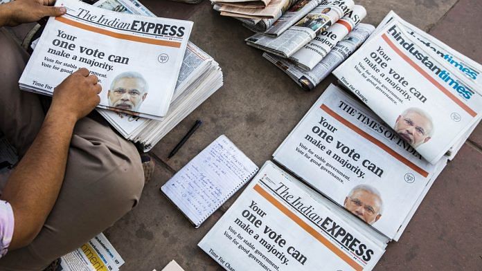 A vendor arranges copies of newspapers that feature a BJP ads picturing Narendra Modi
