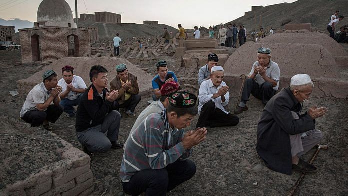 Uyghur men perform prayers for ancestors at a cemetery before the Corban Festival