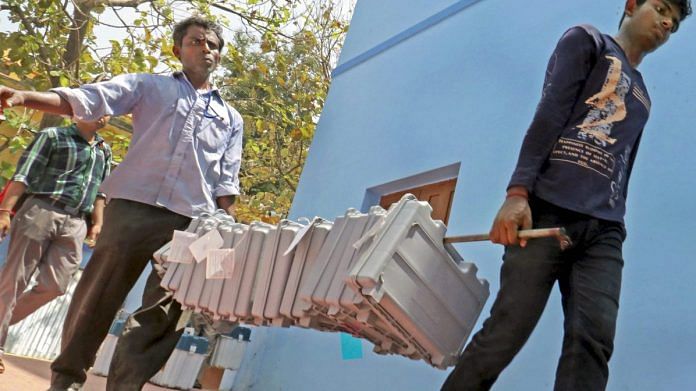 Poll workers carry EVMs at a distribution centre