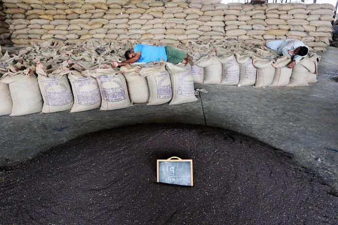 Workers rest on bags of mustard seeds at a wholesale grain market in Rewari, Haryana.