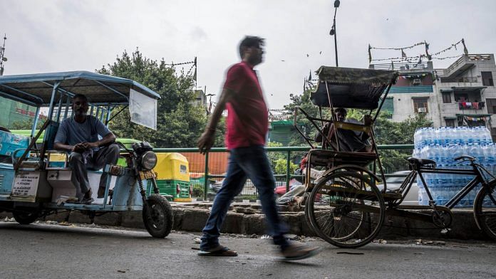 A pedestrian walks past an e-rickshaw and a cycle rickshaw at a stand in New Delhi