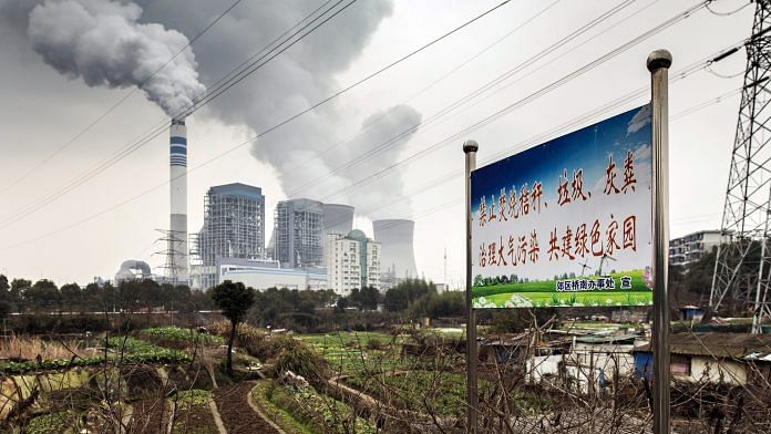 A sign warning local residents not to burn trash in order to reduce pollution stands in a field as emissions rise from cooling towers at a coal-fired power station in Tongling, Anhui province, China. | Photographer: Qilai Shen | Bloomberg