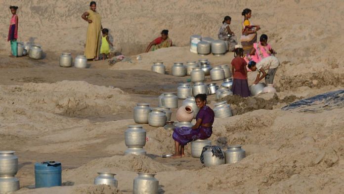 Village women wait with their metal pitchers for the water to get filled in the holes they dug in a dried-up pond during this summer in Palletummalapalem village near Machilipatnam in Andhra Pradesh