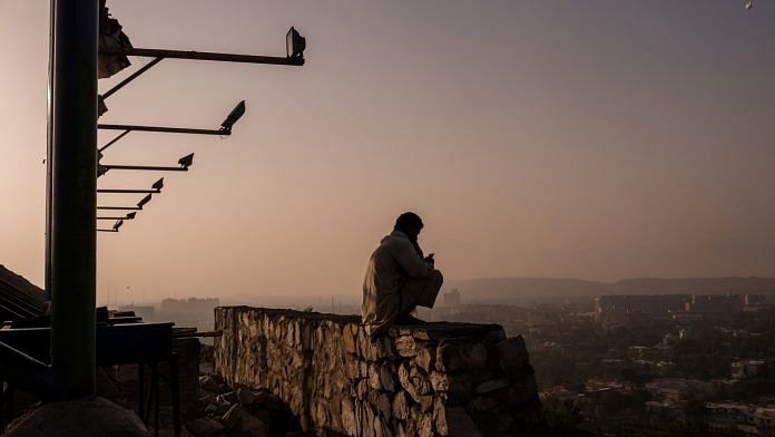 A man is silhouetted as he sits on a wall at the top of Bibi Mahru Hill in Kabul