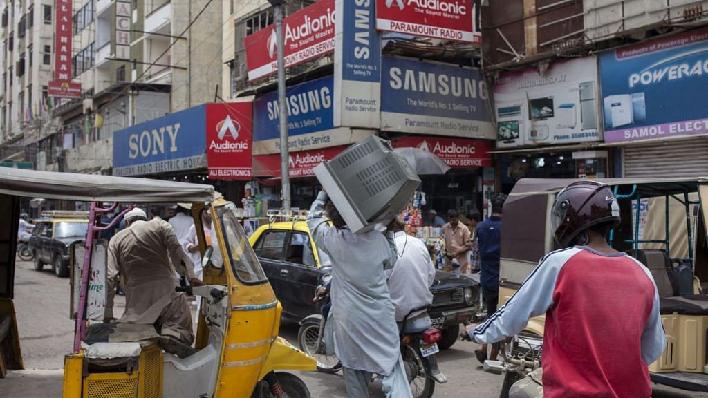 A man carries television set on his shoulder, while walk past an electronic market in Karachi, Pakistan(representational image) | Photographer: Asim Hafeez | Bloomberg