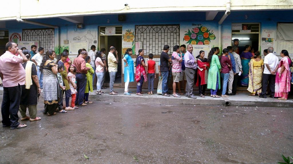 Voters stand in a queue displaying their voter card outside a polling station during Maharashtra Assembly elections in Thane | PTI