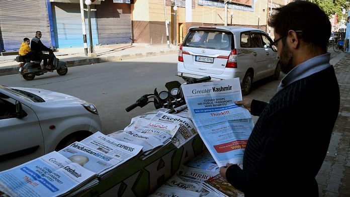 A man reads a newspaper in front of a closed market carrying advertisements against the shutdown in Srinagar. | ANI