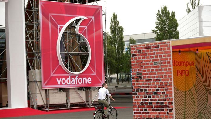 A cyclist rides passed a Vodafone Group Plc logo at the company's exhibition space during the CeBIT 2018 tech fair in Hanover, Germany. | Photographer: Kriztian Bocsi | Bloomberg