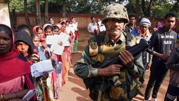 A security jawan keeps vigil as people wait in queues to cast their votes at a polling station during the first phase of Jharkhand Assembly elections. | PTI