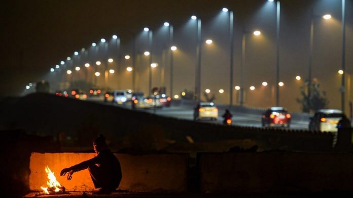 A man warms himself by a bonfire as cars ply in the background on a cold and wintry night, in New Delhi, Friday, Dec. 27, 2019. | PTI