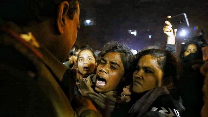 Students protest outside the JNU main gate while a policeman restrains them