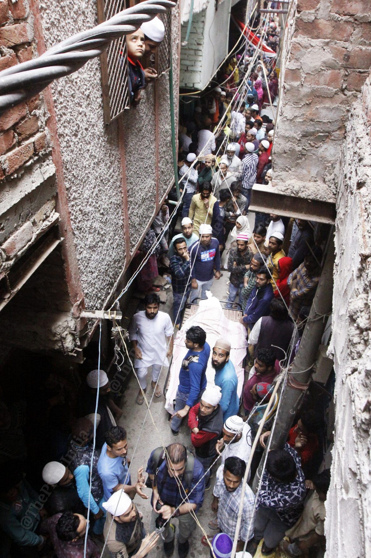 As the bodies reach their residence, hundreds gather to take them out from the van. Bodies being escorted to their residence inside a narrow bylane | Photo: Praveen Jain | ThePrint