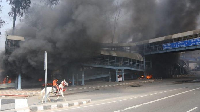 Smoke rises from a foot overbridge at Gokulpuri in Northeast Delhi after rioters indulged in arson