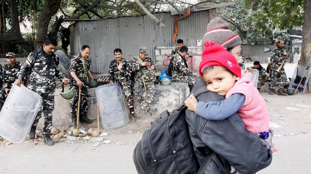 A man carries an infant away from Mustafabad in Northeast Delhi as police personnel look on | Photo: Praveen Jain | ThePrint