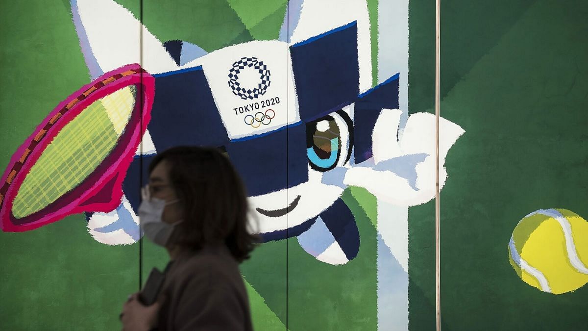 Woman wearing a mask crosses a Tokyo Olympics sign | Bloomberg