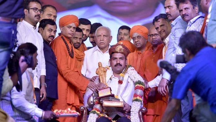File photo of Vijayendra (seated) with his father Yediyurappa (standing behind him) at the religious convention | Twitter: @BYVijayendra