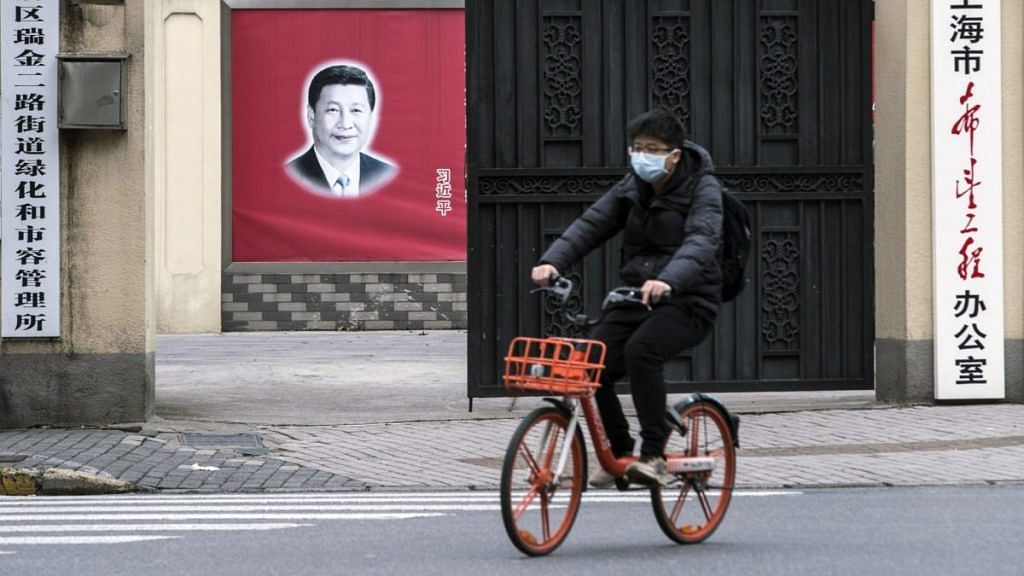 A cyclist wearing a protective mask rides past a banner of Chinese president Xi Jinping in Shanghai | Qilai Shen/Bloomberg