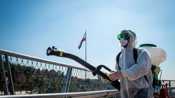 A firefighter wearing protective clothing, mask and goggles, sprays disinfectant on Tabia't bridge pedestrian overpass in Tehran, Iran