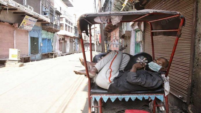 A rickshaw puller wearing a mask dozes off during a COVID-19 lockdown