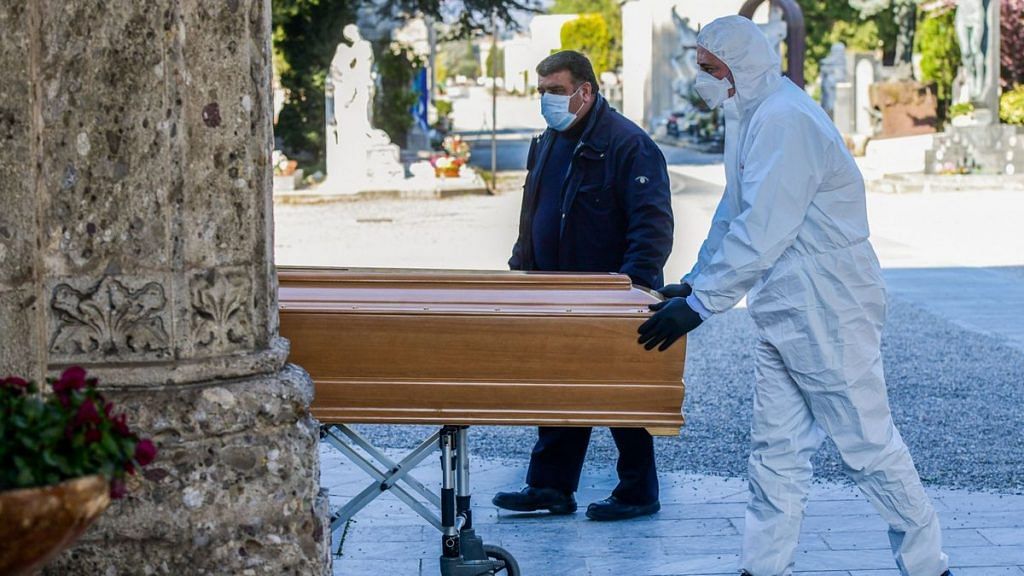 An undertaker wearing a face mask and overalls unloads a coffin out of a hearse on March 16, 2020 at the Monumental cemetery of Bergamo, Lombardy. | Photographer: Piero Cruciatti | AFP via Getty Images | Bloomberg