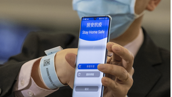 An official shows a bracelet and complementary tracking app that will be given to inbound travelers requiring compulsory home-quarantine at Hong Kong International Airport (HKG) on March 18. | Bloomberg