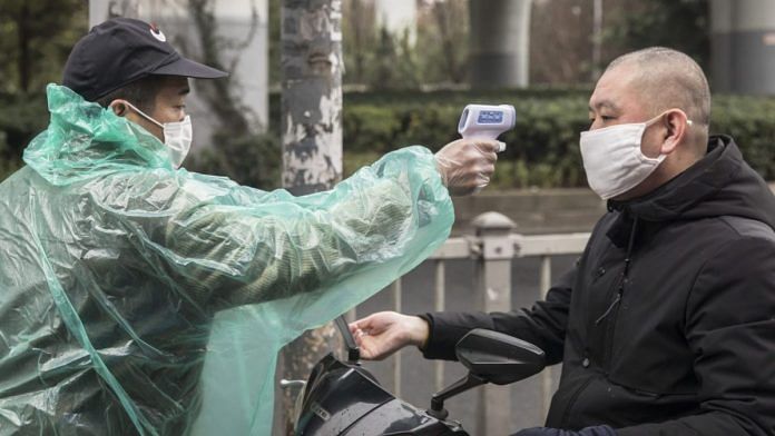 A security guard takes the temperature of a man wearing a protective mask at an entrance to a fresh produce market in Shanghai, China, on 15 February 2020 | Photo: Qilai Shen | Bloomberg