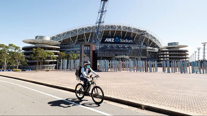 A cyclist wearing a protective mask rides past the closed ANZ Stadium during a partial lockdown imposed due to the coronavirus in Sydney, Australia. | Photographer: Brendon Thorne | Bloomberg