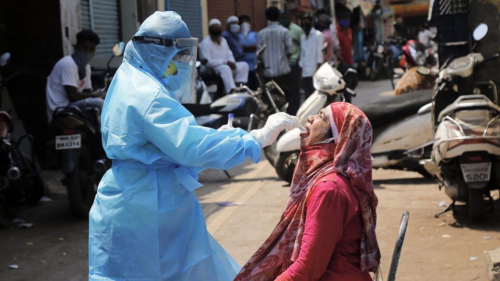 A medic collects swab from the mouth of a woman resident for COVID-19 test in a containment zone at Kurla, Mumbai, Tuesday, April 14, 2020. | PTI
