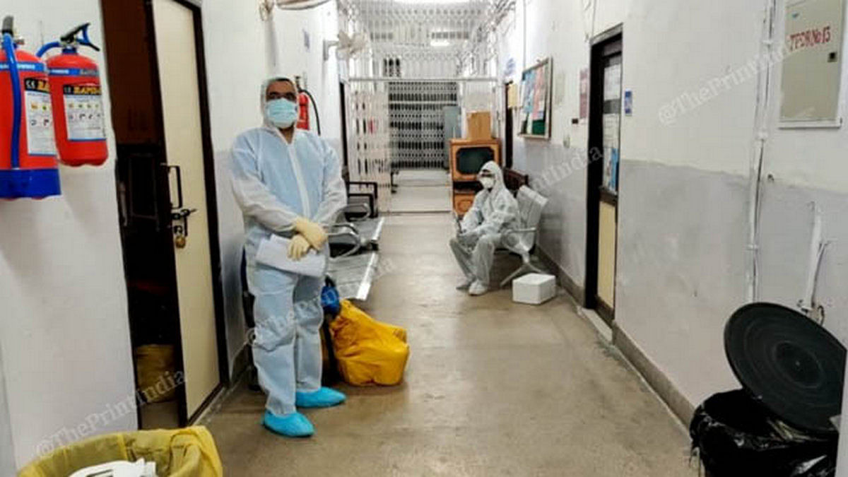 Two men in protective gear wait outside the lab with new samples (in yellow pack) | Photo: Angana Chakrabarti | ThePrint