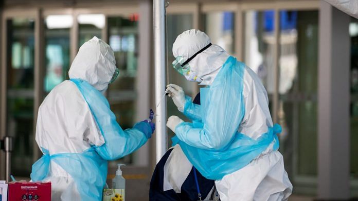 Medical staff in protective gear collect a sample from an arriving passenger at a coronavirus testing station at Incheon International Airport in Incheon, South Korea | Photographer: SeongJoon Cho | Bloomberg