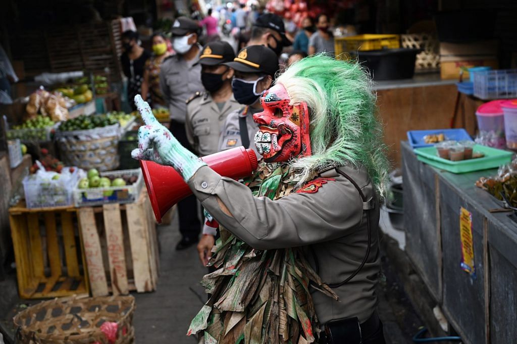 A police officer wears a mask called "Leak" while educating people on coronavirus matter at a market in Kerobokan | Photographer: Sonny Tumbelaka/AFP via Getty Images
