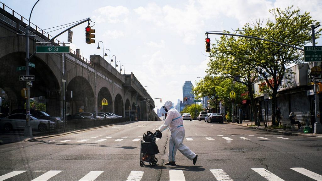 A man wearing a protective suit crosses a street in Queens, New York City on May 15. | Bloomberg