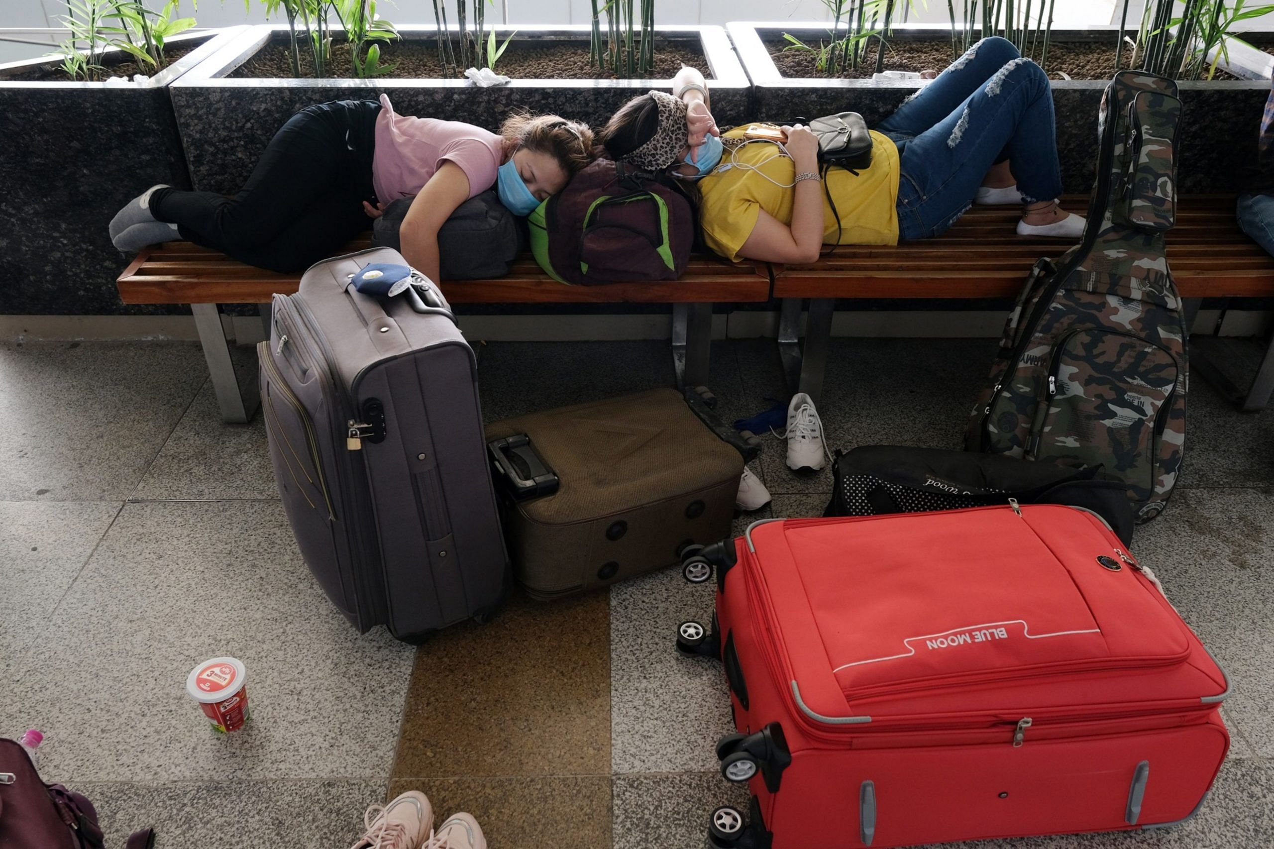 Travelers rest on benches at Delhi Airport on May 25 | Bloomberg