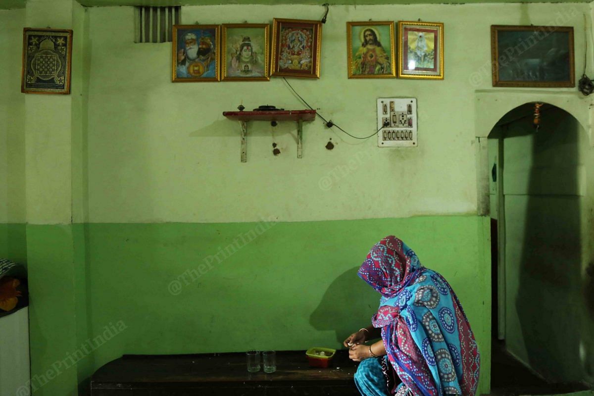 A women does some chores in a room where there are photographs of gods from different religion | Photo: Manisha Mondal | ThePrint