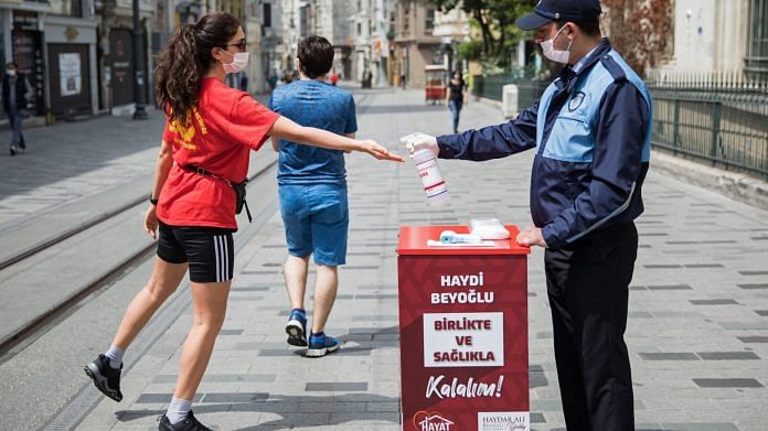 A municipal worker squirts hand sanitizer into the hand of a pedestrian in Istanbul on May 14. | Bloomberg